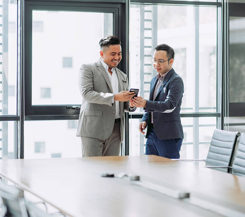 Image of two men looking at phone in a boardroom.